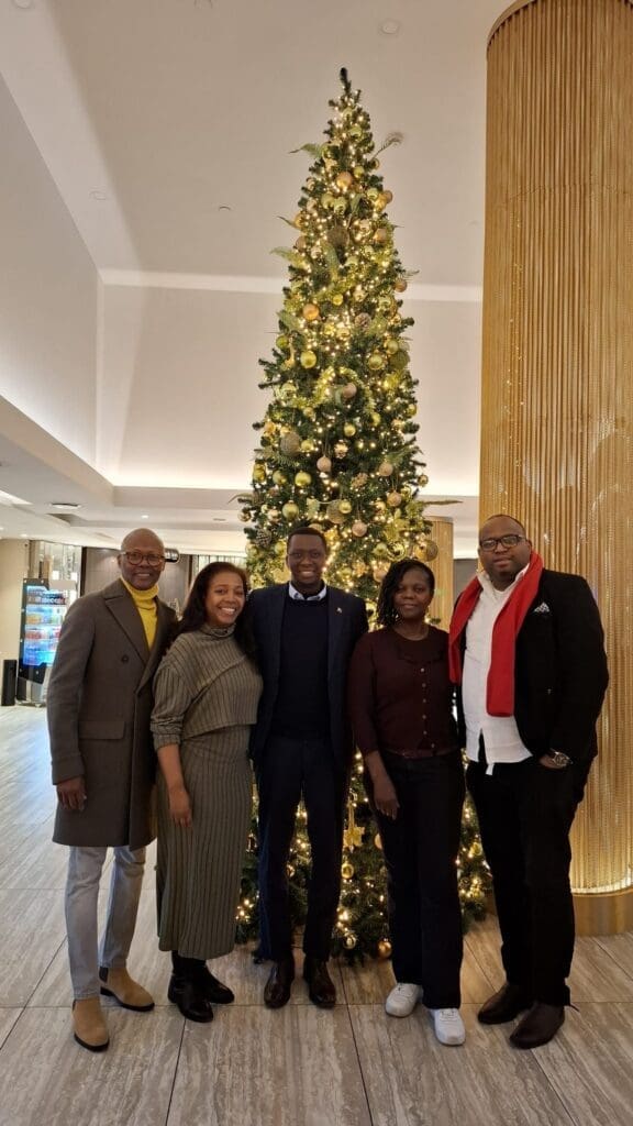 A group of five individuals standing in front of a beautifully decorated Christmas tree, representing a meeting in Brussels focused on collaboration and advocacy for people of African descent.